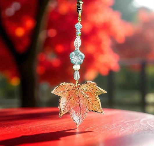 Decorative leaf charm with beads against a blurred autumn background