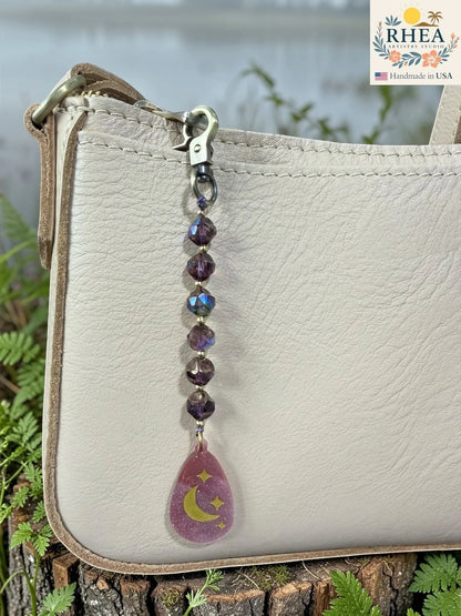amethyst mist Handmade beaded bag charm with violet-toned glass beads and hand-painted pendant photographed outdoors