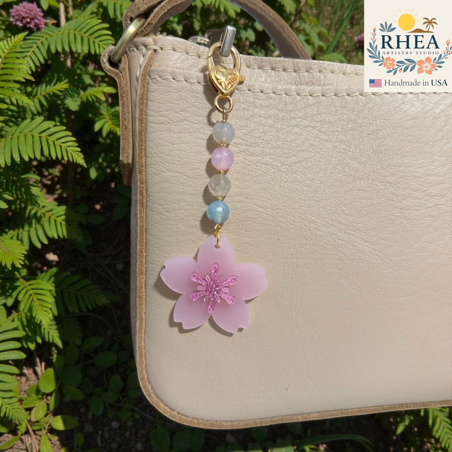 Handbag with a pink flower charm and beads, set against a natural background. Handmade floral bag charm with pastel glass beads and gold hardware