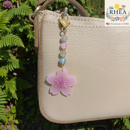 Handbag with a pink flower charm and beads, set against a natural background. Handmade floral bag charm with pastel glass beads and gold hardware