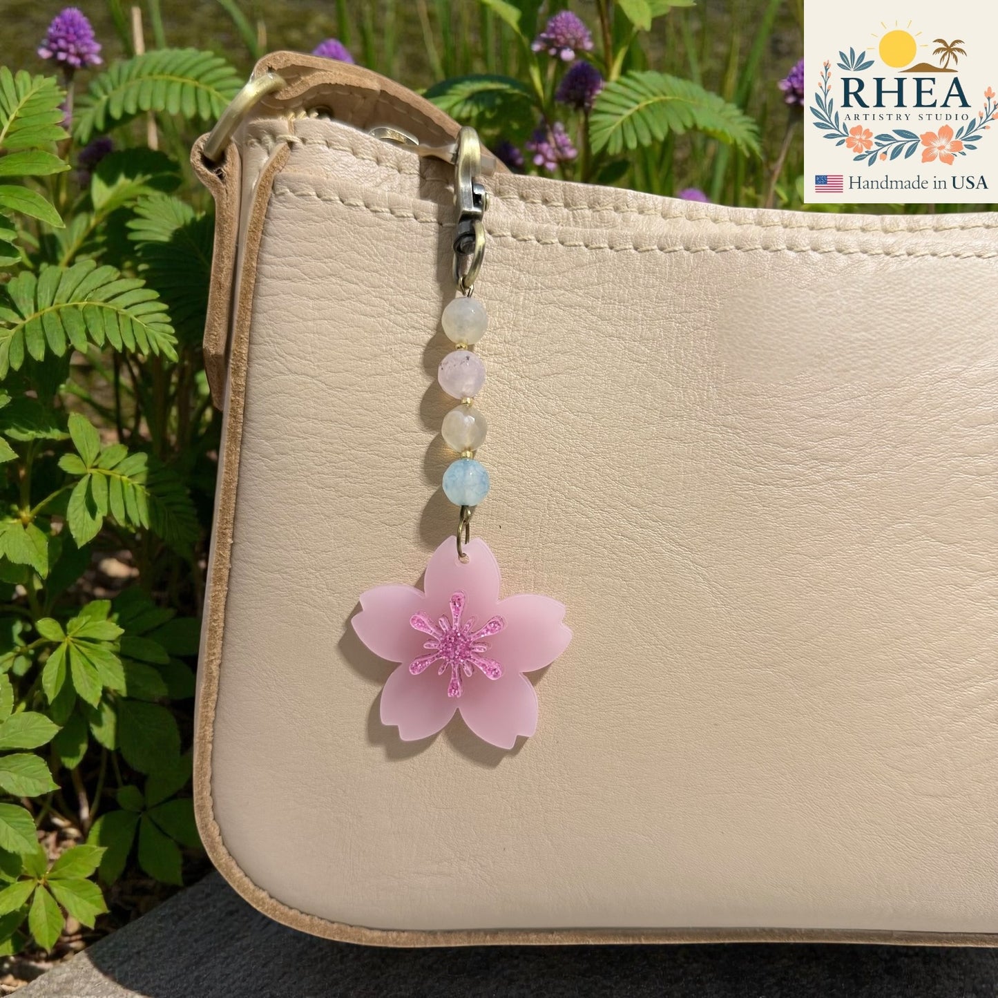 Beaded keychain with a pink flower charm attached to a beige bag, with greenery in the background. Floral beaded zipper charm with pink blossom pendant, handmade in USA