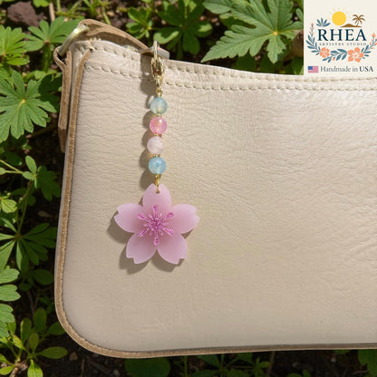 Decorative charm with a pink flower and beads on a beige pouch against a natural background, Cherry blossom beaded bag charm with frosted pink floral pendant on leather bag