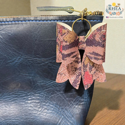 Butterfly-shaped purse charm attached to a blue textured bag with RHEA branding.