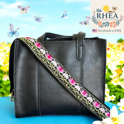 Black leather handbag with floral purse strap against a colorful background, featuring the RHEA Artistry Studios logo.