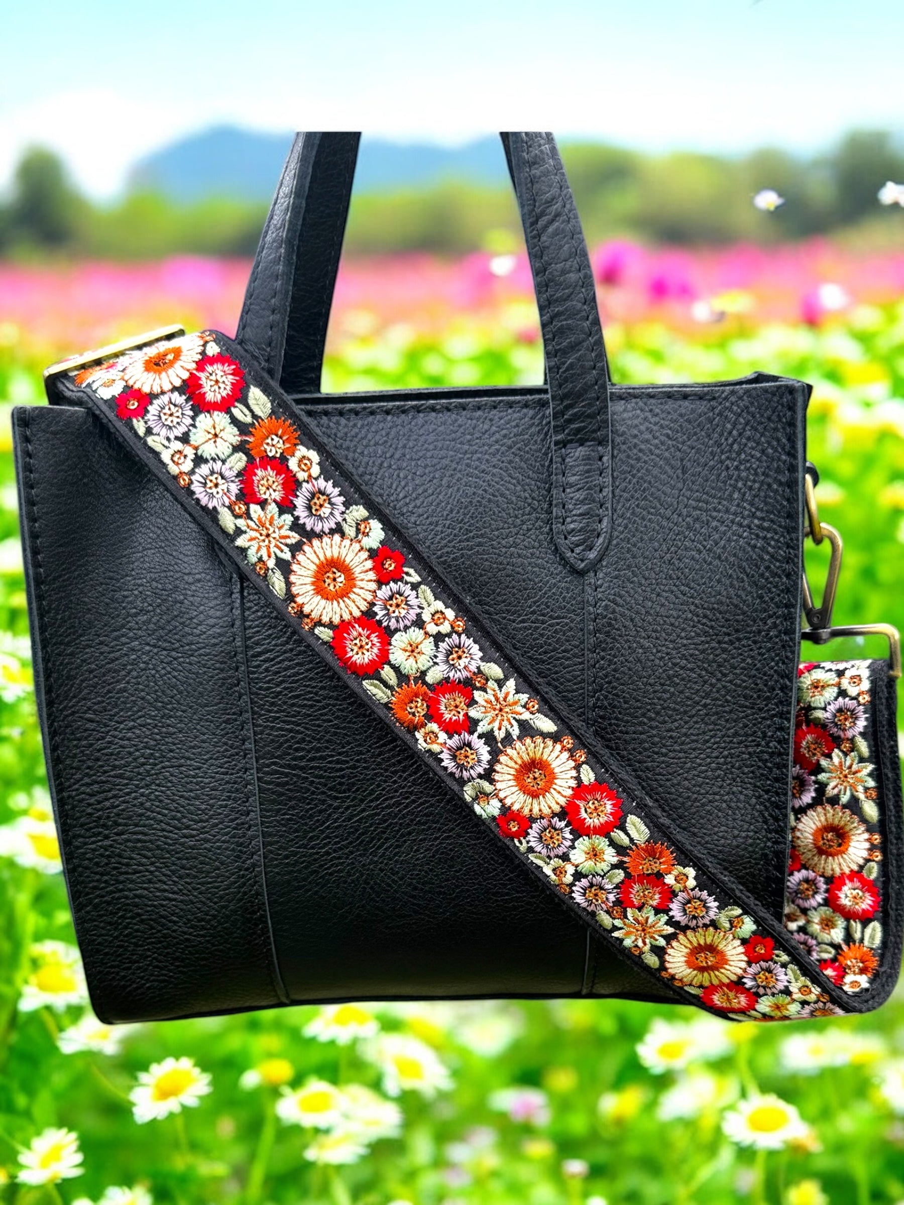 A floral embroidered purse strap in multicolor, attached to a black leather bag with brushed brass hardware.