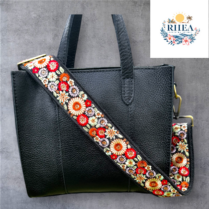 A floral embroidered purse strap in multicolor, attached to a black leather bag with brushed brass hardware.