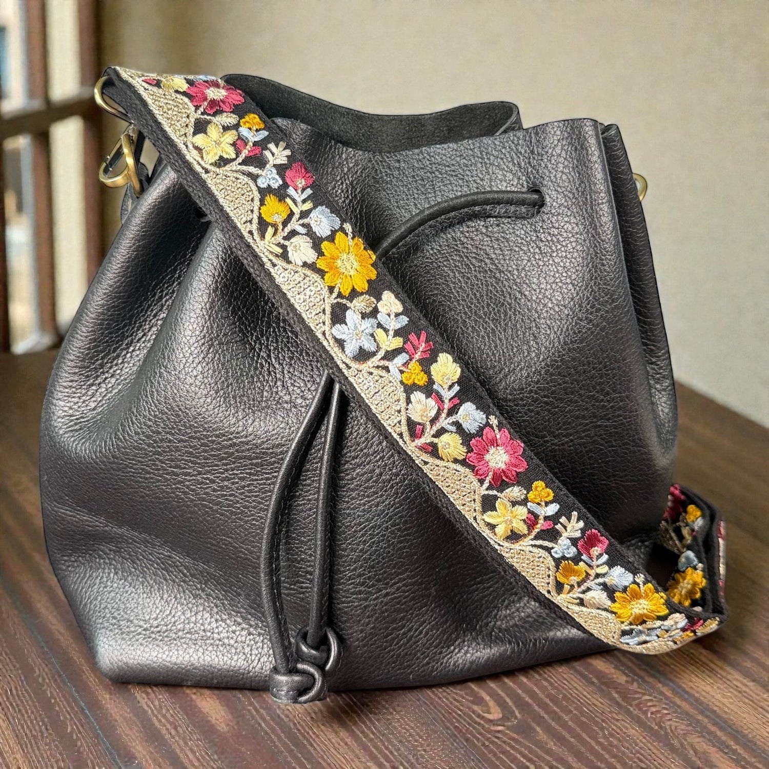 black Embroidered strap attached to a handbag, 1.5 inch wide, Black leather handbag with floral embroidery strap on a wooden surface