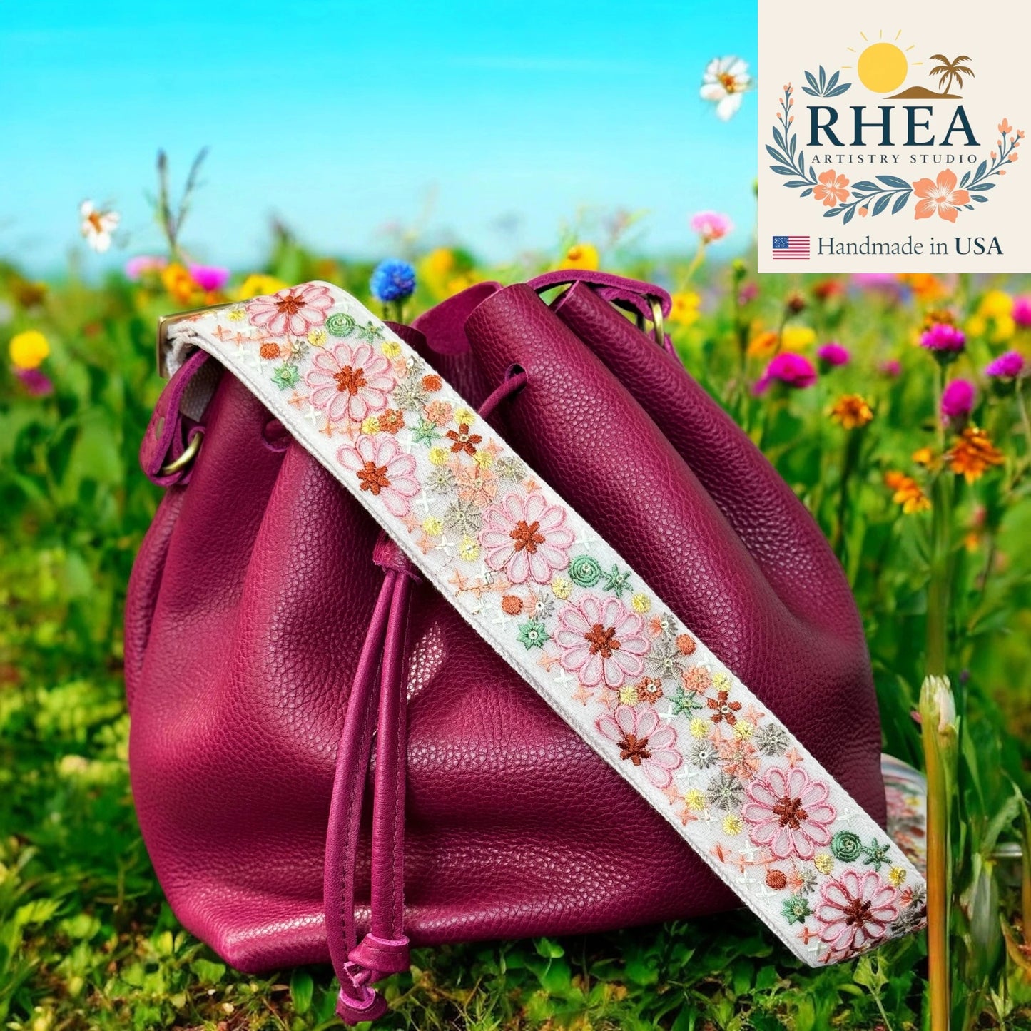 Purple leather bag with a floral strap in a field of flowers, featuring the Rhea Artistry Studio logo.