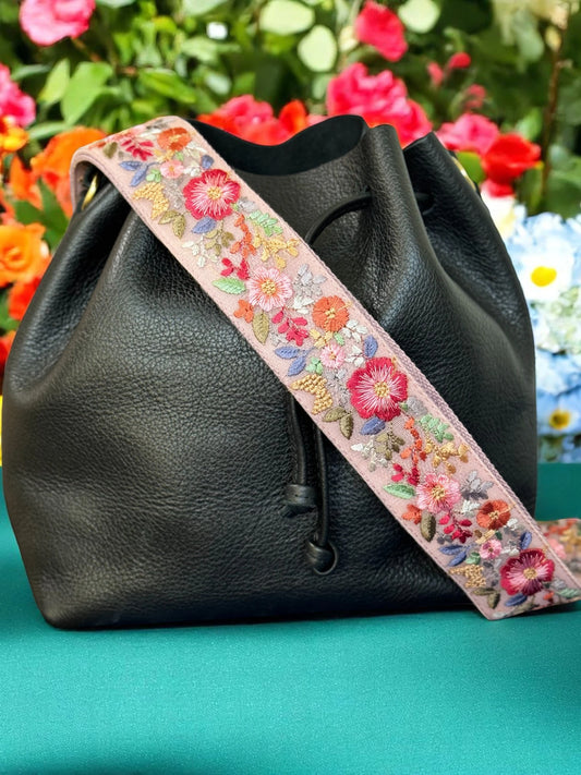 Bloomcraft Orchard Blush Strap styled among blooming garden flowers – vibrant floral embroidery in coral, lilac, and gold on a soft pink base.