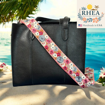 Black handbag with a floral purse strap against a bright blue background, featuring the Rhea Artistry Studio logo.
