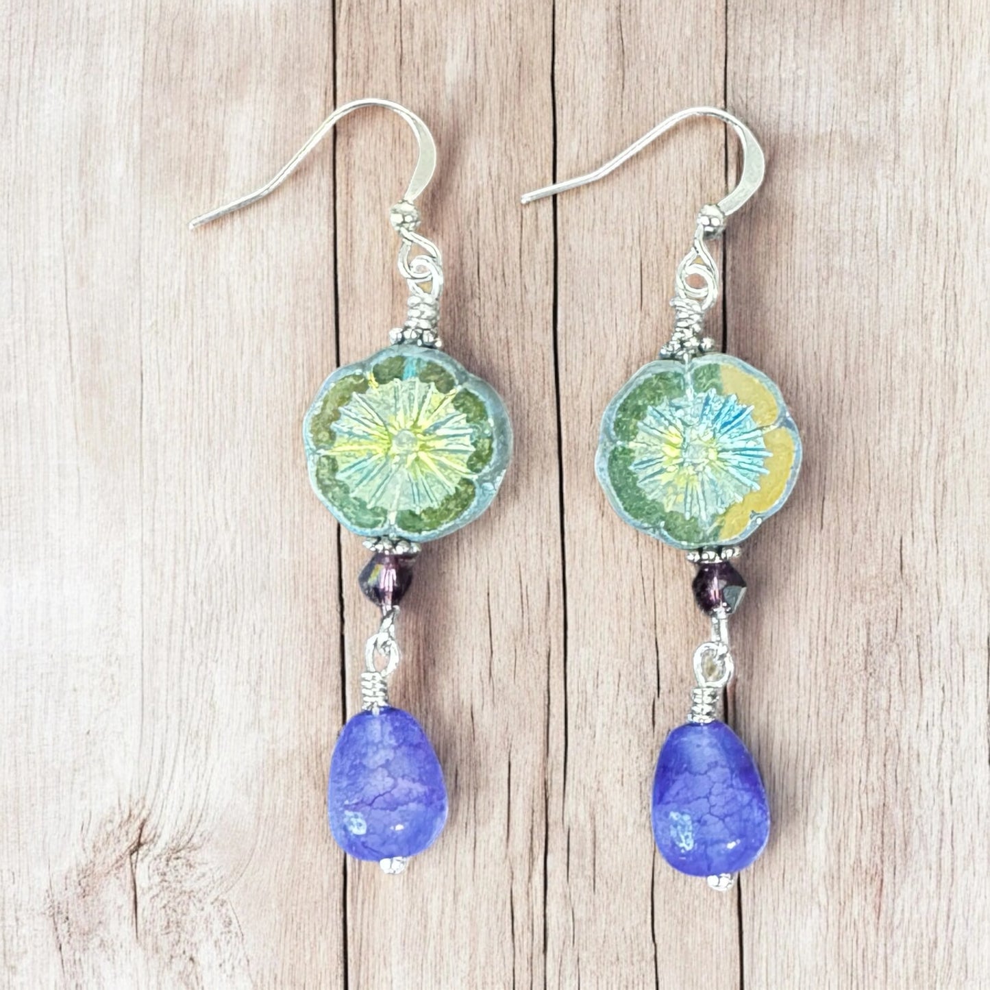 Pair of earrings with green floral designs and purple beads on a wooden surface