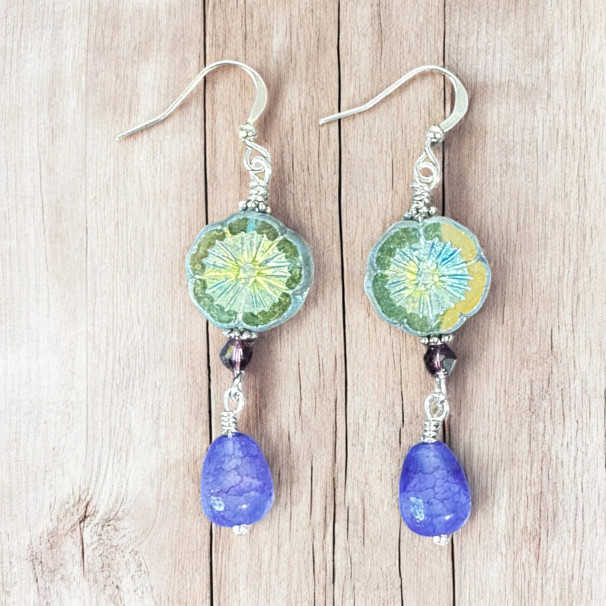 Pair of earrings with green floral designs and purple beads on a wooden surface