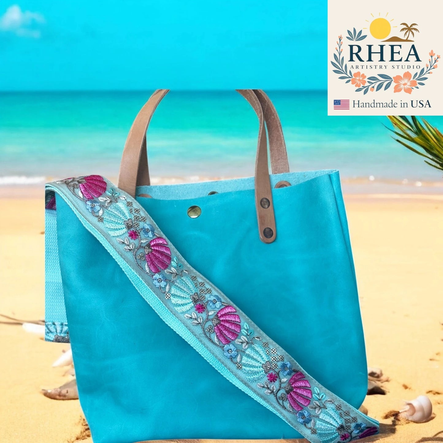 Turquoise tote bag with decorative strap on a beach, featuring the RHEA Artistry Studio logo.