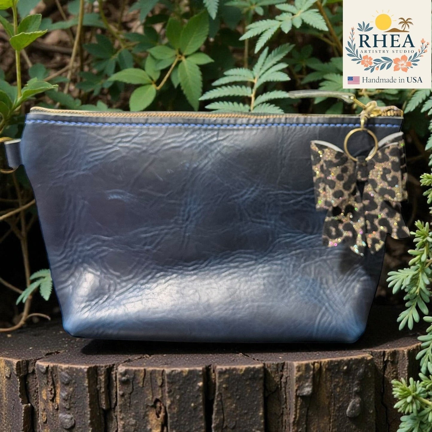 Blue leather pouch with floral bag charm on a wooden stump with greenery