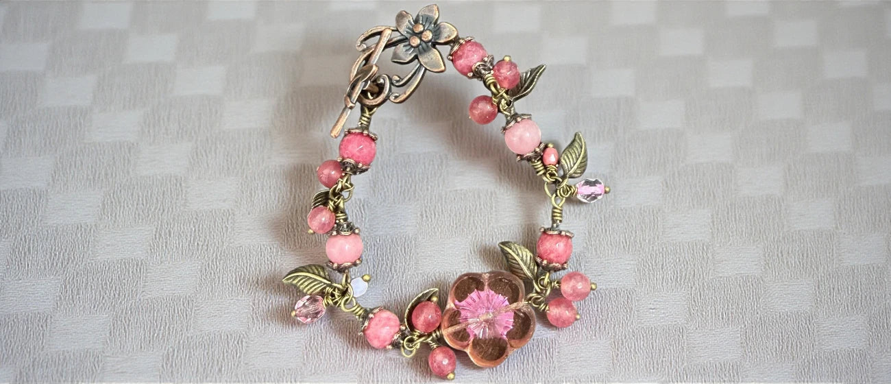 Decorative bracelet with pink flowers and green leaves on a textured gray background