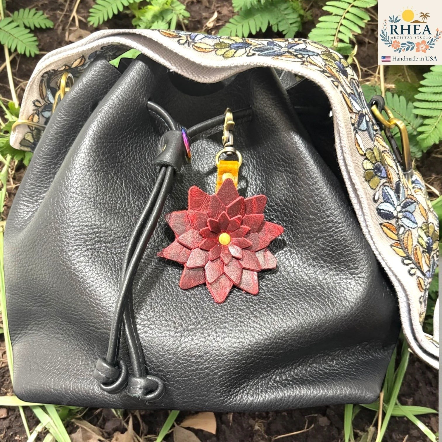 Black leather bag with a red floral keychain against a natural background , Deep wine red leather starflower charm handmade in the USA