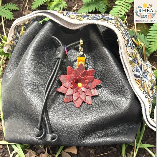 Black leather bag with a red floral keychain against a natural background , Deep wine red leather starflower charm handmade in the USA