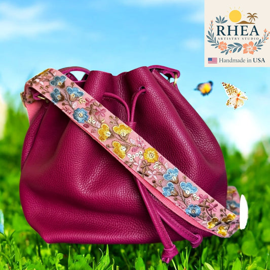 Pink leather bag with floral purse strap on grass, RHEA Artistry Studio logo visible