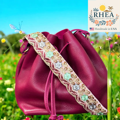 Pink leather bag with floral strap against a natural background, featuring the Rhea Artistry Studio logo.