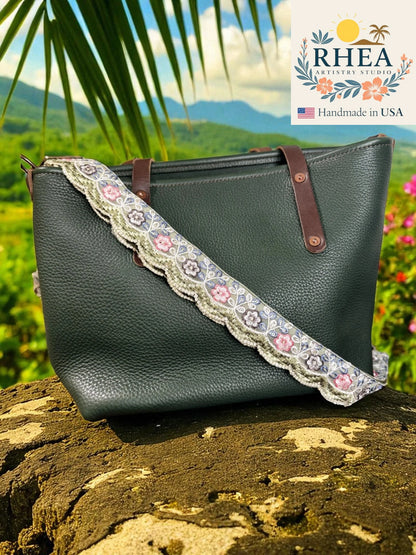 Green handbag with floral lace strap on a rock with a scenic background, featuring the RHEA Artisan Studio logo.