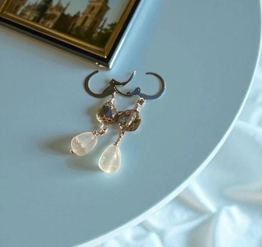 Gold earrings with teardrop-shaped stones on a light blue surface