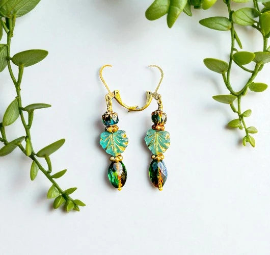 Pair of gold and green earrings on a white background with green leaves.
