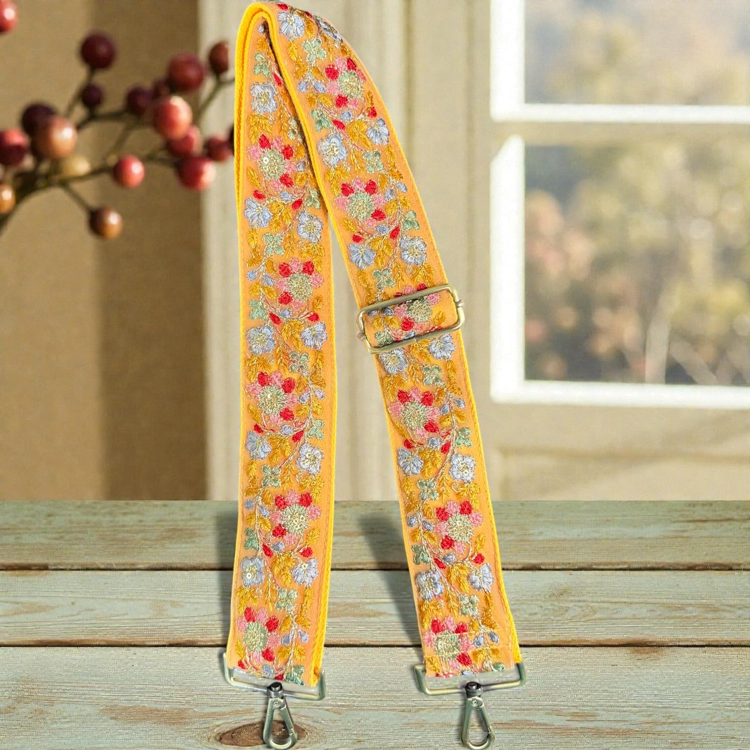 Brushed brass hardware on handmade embroidered strap, Floral patterned strap on a wooden surface with a blurred background