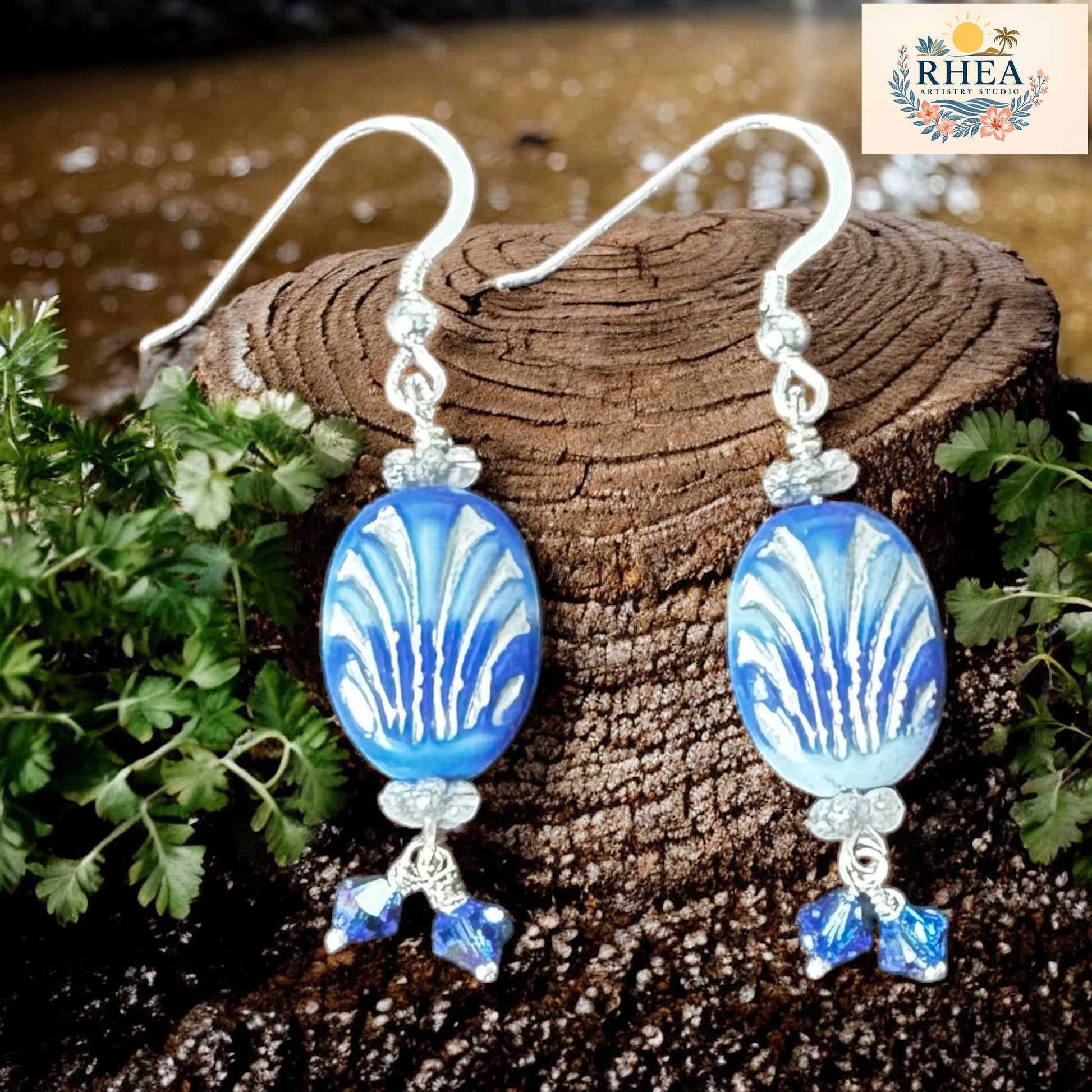 Blue and white patterned earrings on a wooden surface with RHEEA branding.