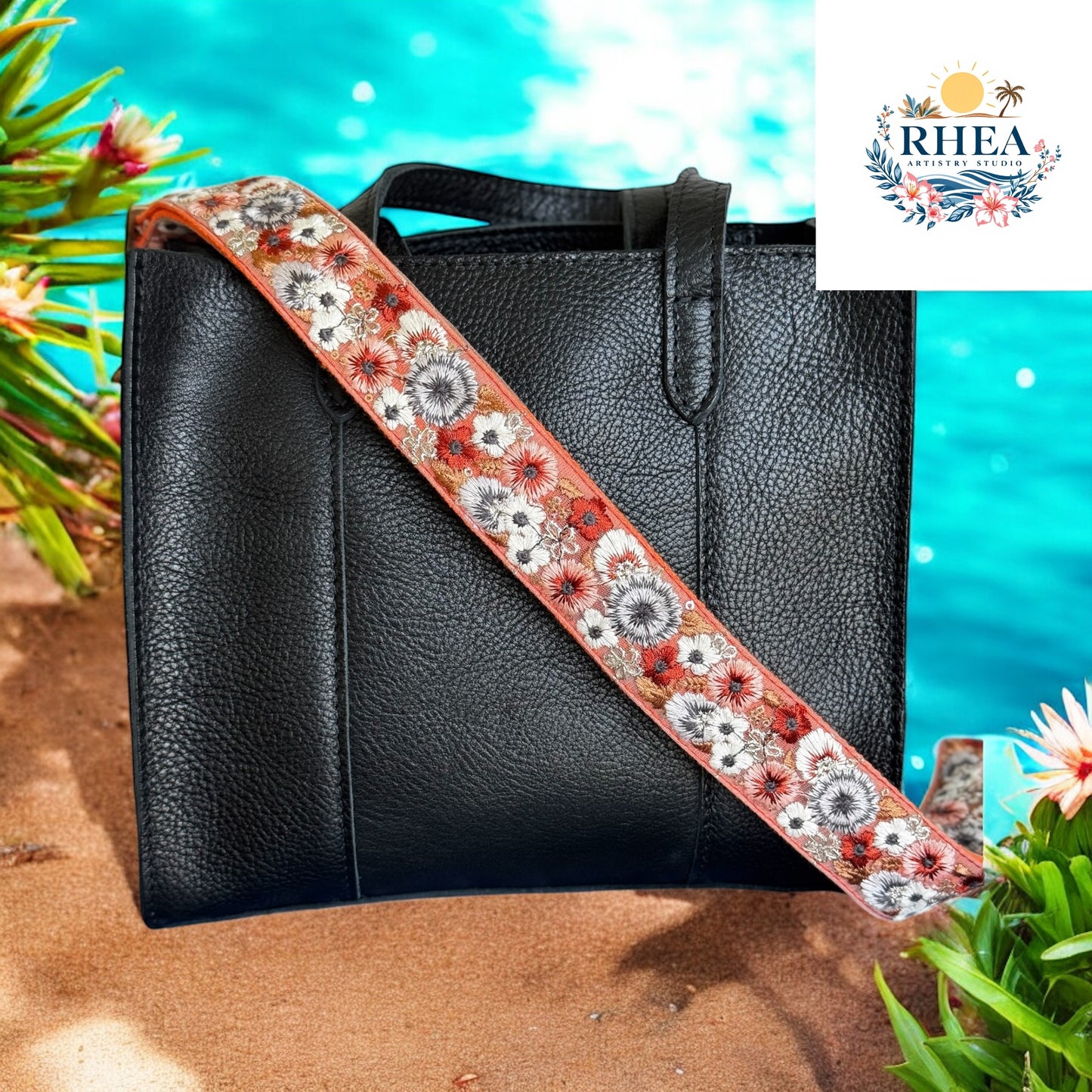 Black leather handbag with a coral embroidered strap featuring black, white, and rust-colored flowers, styled against a blooming field backdrop.