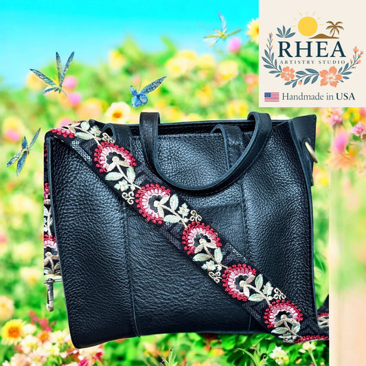 Black handbag with decorative purse strap against a colorful outdoor background, featuring the RHEA Artistry Studio logo.