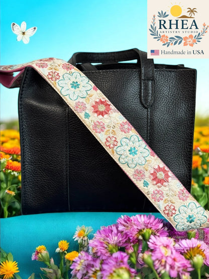 Black handbag with a floral purse strap against a colorful floral background, featuring the RHEA Artisan Studio logo.