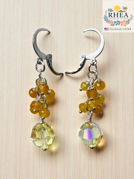 Pair of earrings for women with citrine beads and a large clear bead on a wooden surface, branded 'RHEA'.