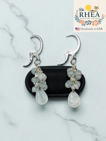 Pale blue earrings for women with clear stones on a marble surface, branded 'RHEA Artistry Studio'.