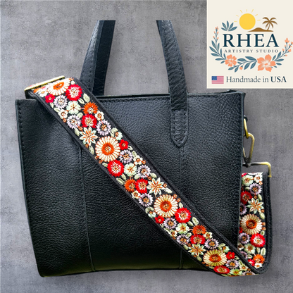Black handbag with a colorful floral purse strap on a gray background, featuring the Rhea Artistry Studio logo.