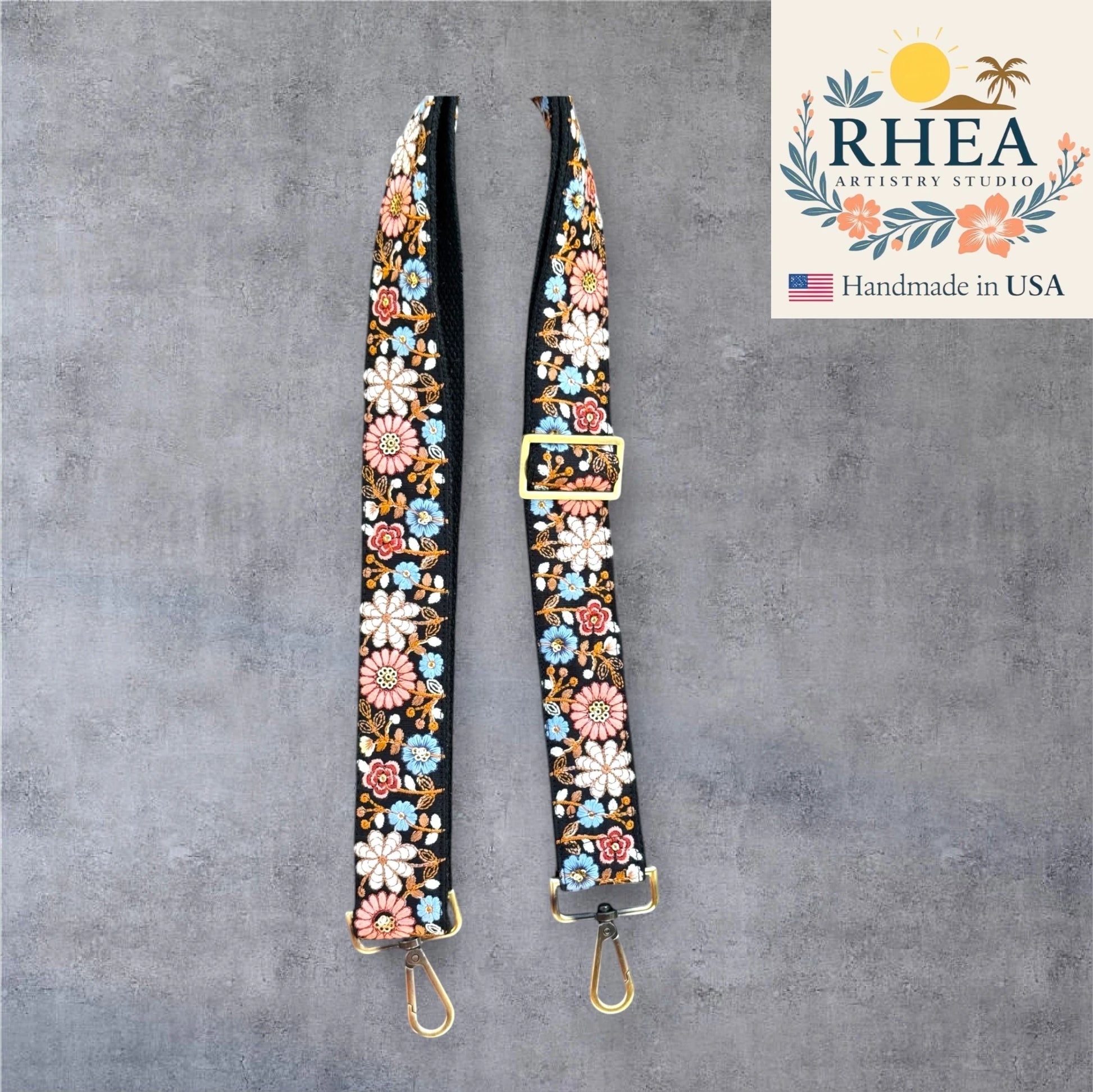Floral embroidered bag purse strap with gold buckles on a gray background, featuring the RHEA Artistry logo.