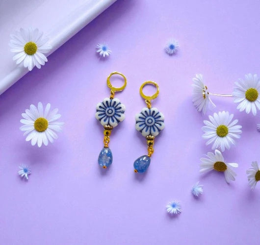 Pair of earrings with floral designs on a purple background with daisies.