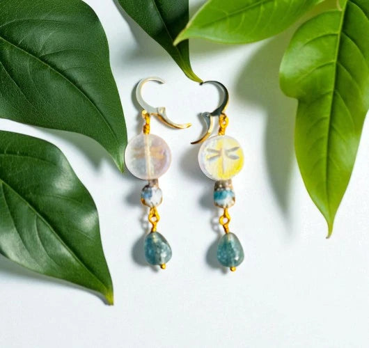 Pair of earrings with green and gold beads on a white background with green leaves.
