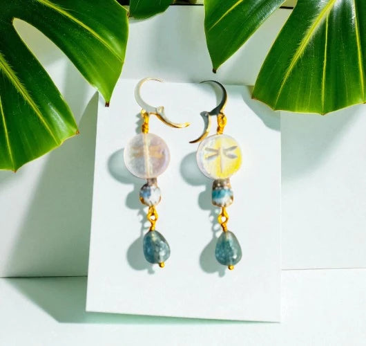 Pair of earrings with colorful beads on a white card with green leaves in the background
