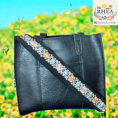 Black leather handbag with floral strap against a colorful floral background, featuring the RHEEA brand.