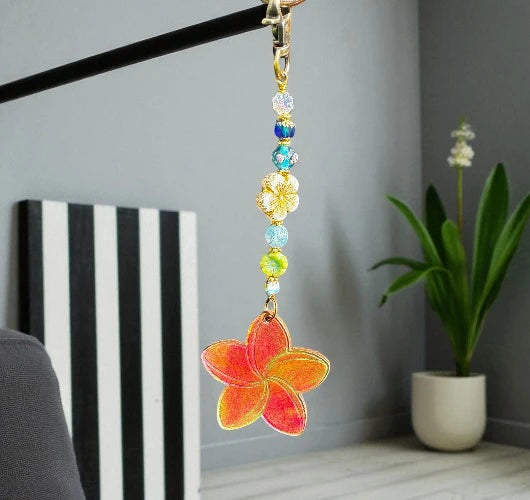 Decorative keychain with colorful beads and a floral design hanging against a neutral background.