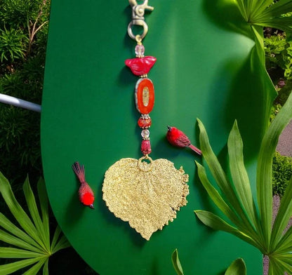 Decorative keychain with gold leaf design and red birds on a green leaf background