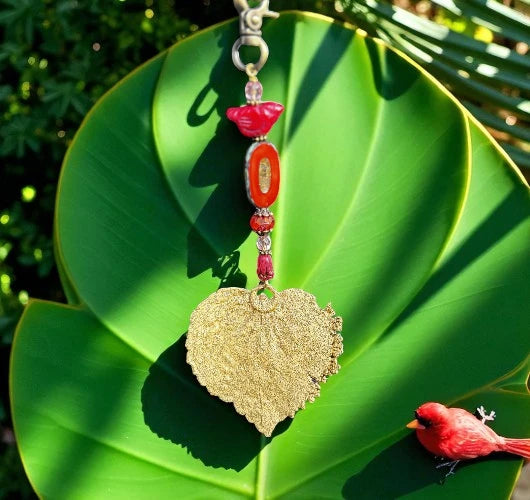 Decorative keychain with gold leaf and red beads on a green leaf