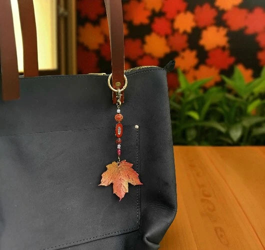 Black handbag with a leaf-shaped charm on a wooden surface with a blurred floral background