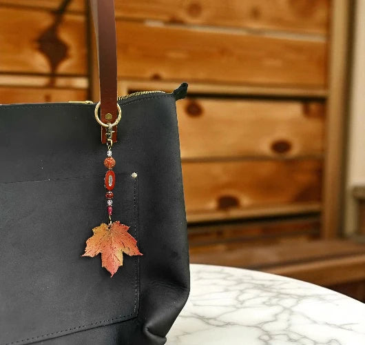 Black tote bag with a leaf-shaped keychain on a marble surface with wooden background