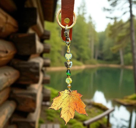 Decorative charm with a leaf design hanging from a leather strap against a scenic background of a lake and forest.