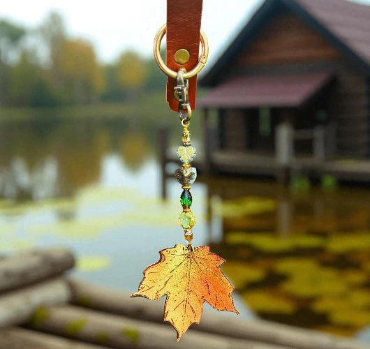 Decorative keychain with a leaf charm in front of a blurred lake and cabin background