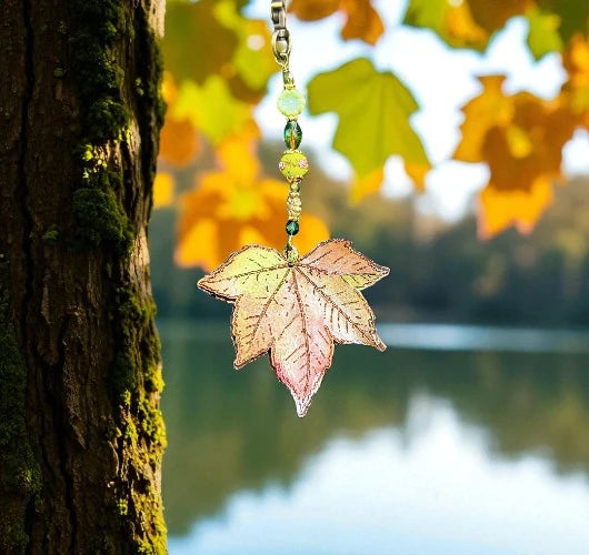 Decorative leaf ornament hanging from a tree with a blurred autumn scene in the background.