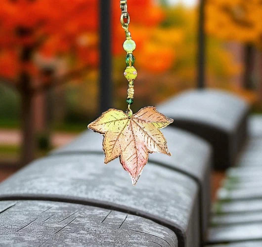 Leaf-shaped keychain with beads on a blurred autumn background