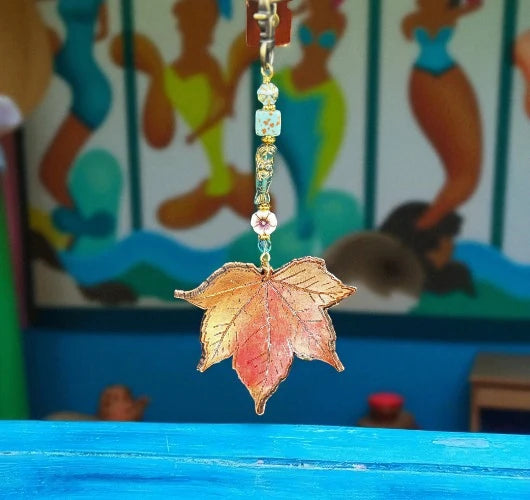 Decorative leaf charm with beads on a blue surface, colorful background