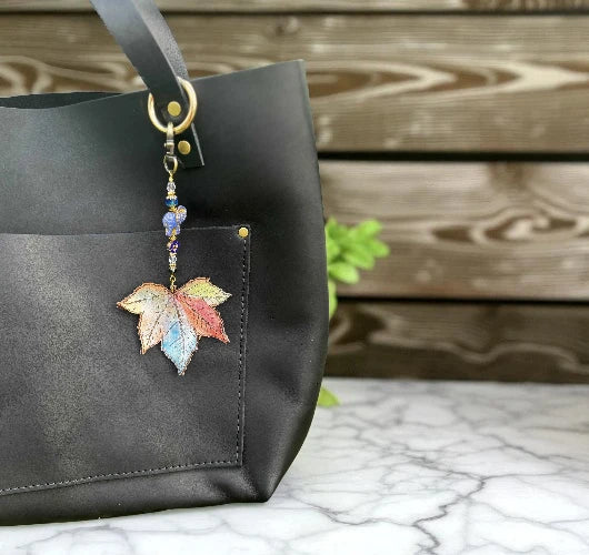 Black handbag with a colorful leaf-shaped keychain on a marble surface with a wooden background.